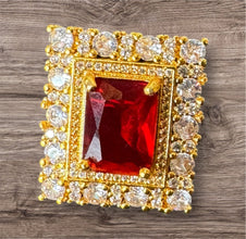 Gold jewelry piece with a red gemstone and clear stones on a wooden surface