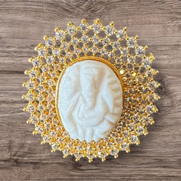 Decorative ring with a central ganesh muga and gold and crystal embellishments on a wooden surface